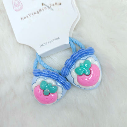 Pair of blue hair ties with pink and green charms on a white background