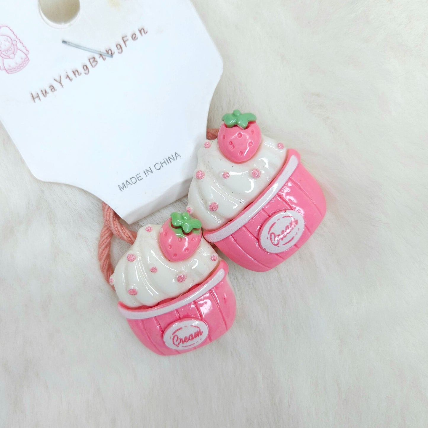 Pink and white dessert-themed hair tie with a matching container on a light background