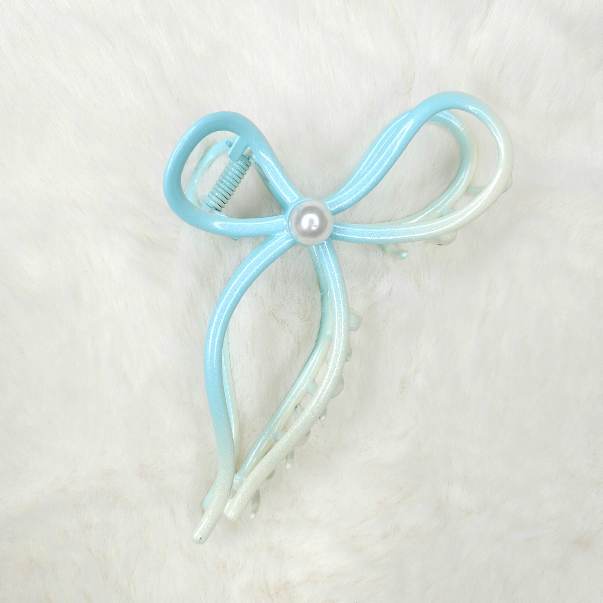 Light blue and white bow-shaped hair clip with a pearl center on a light gray background