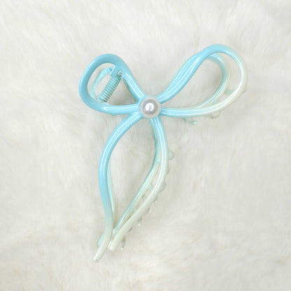 Light blue and white bow-shaped hair clip with a pearl center on a light gray background