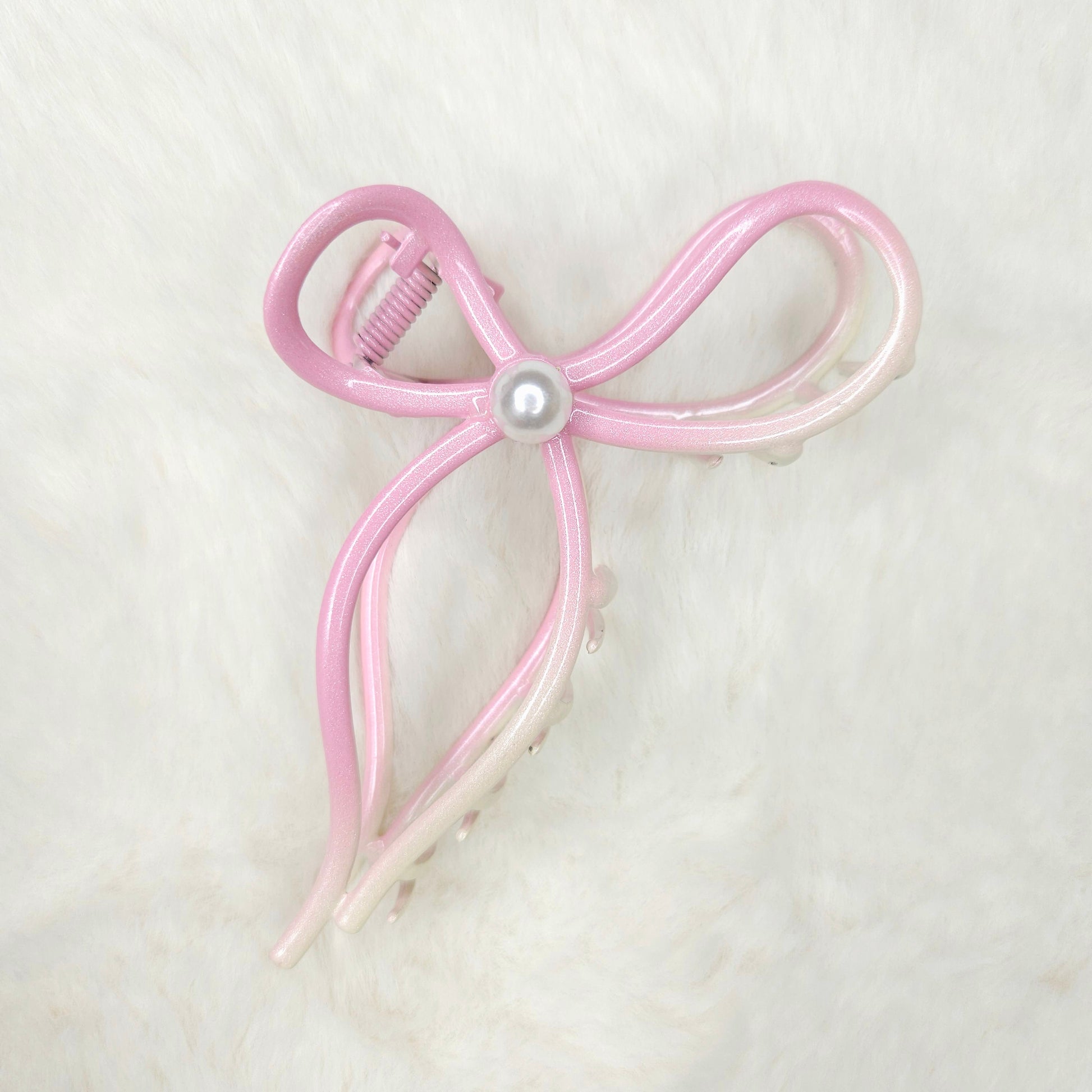 Pink bow-shaped hair clip with a pearl center on a light gray background