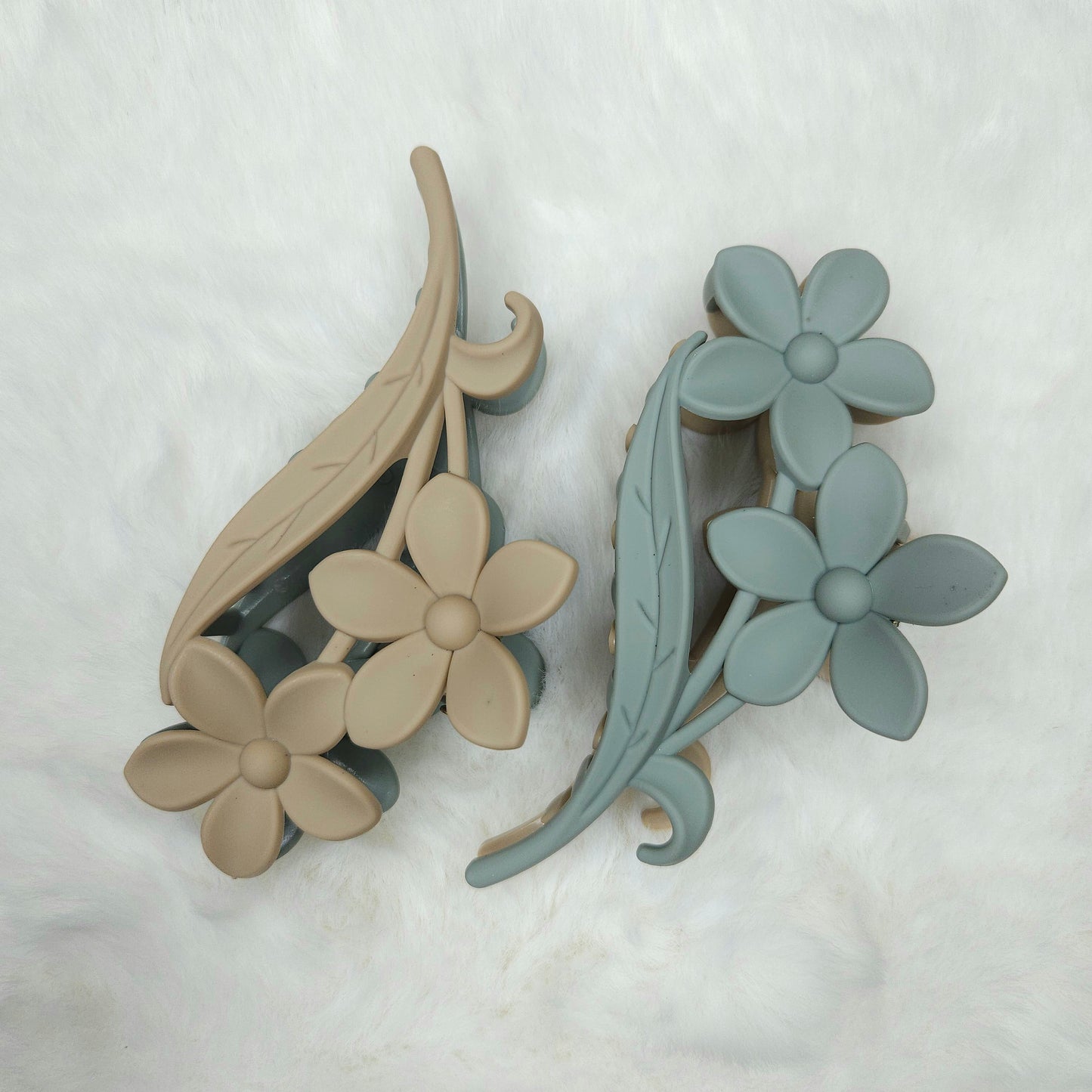 Dual tone light grey and light green hair claw clips with floral details placed on a white background.