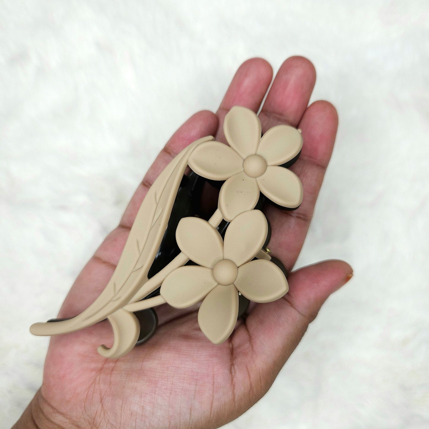 Hand holding a beige floral hair claw clip against a white background