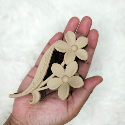 Hand holding a beige floral hair claw clip against a white background