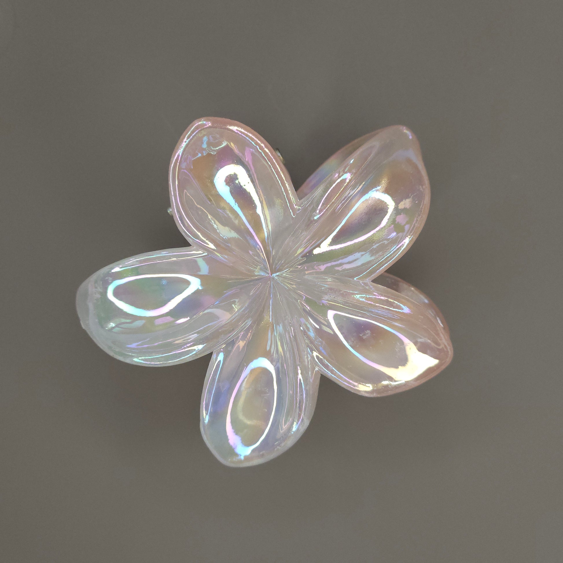 A medium-sized, light orange (peach) flower hair claw clip with a dual-shade glimmer, giving the plastic a pearlescent shine that shifts between pale orange and soft yellow tones.