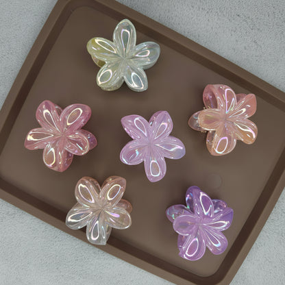 A medium flower-shaped hair claw clip featuring a 'dual shade' design, where the petals transition between two glimmering colors, such as pink and gold, giving it an iridescent effect.