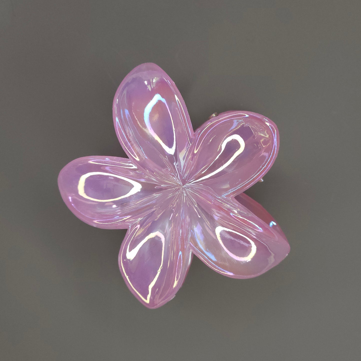 A medium, flower-shaped hair claw clip in a glossy pink color that features a 'dual-shade glimmer,' giving it an iridescent shift between pink and another tone, such as gold or peach.