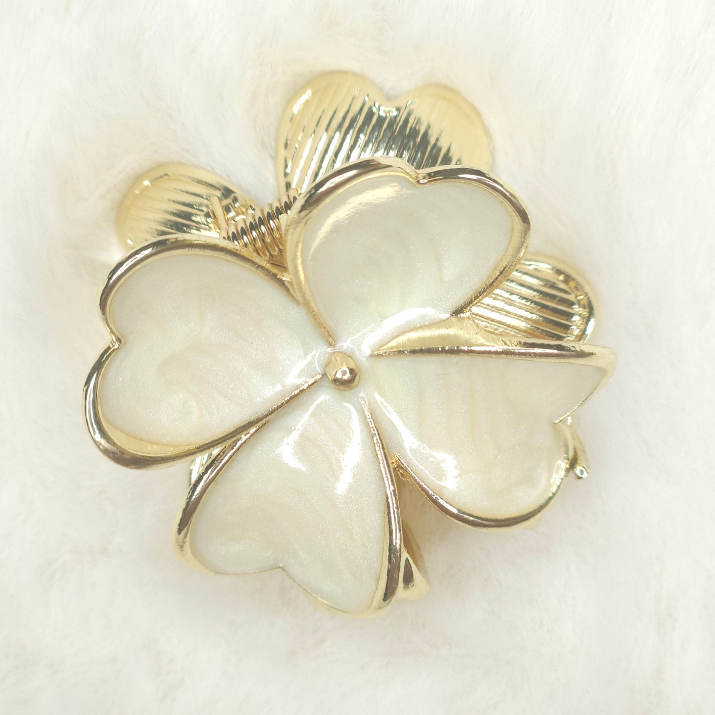 Gold and white four-leaf clover brooch on a light background