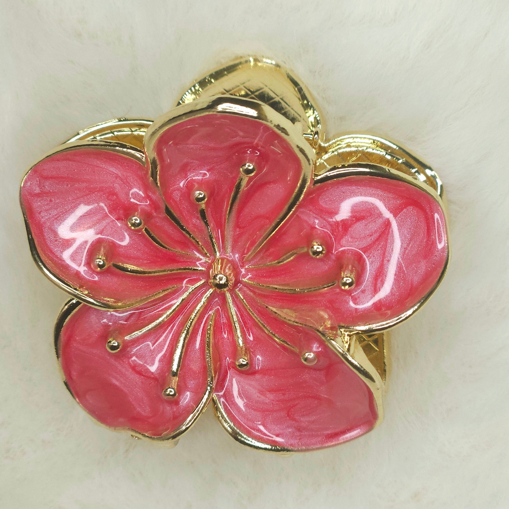 Pink flower-shaped hair claw with gold accents on a light background