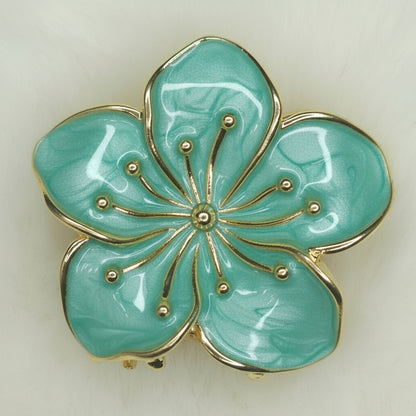 Turquoise flower-shaped hair claw with gold accents on a light background
