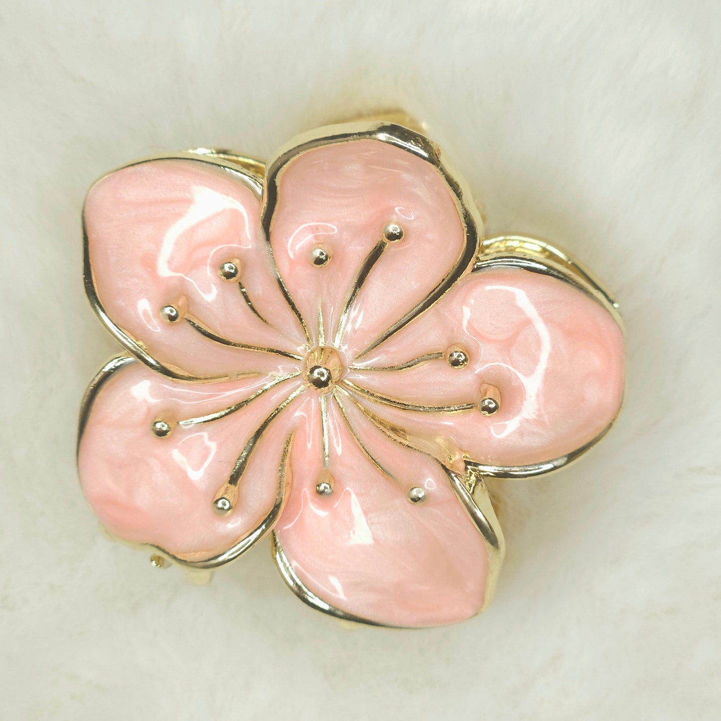 Pink flower-shaped hair claw with gold accents on a beige background