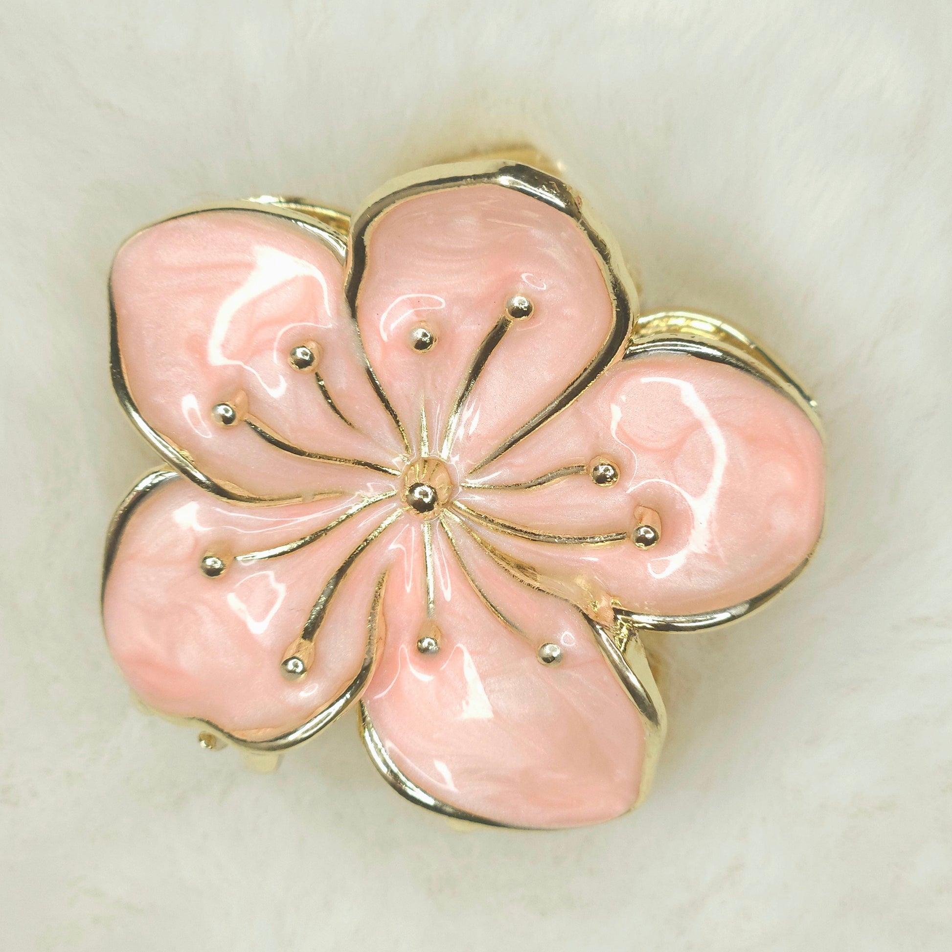 Pink flower-shaped hair claw with gold accents on a beige background
