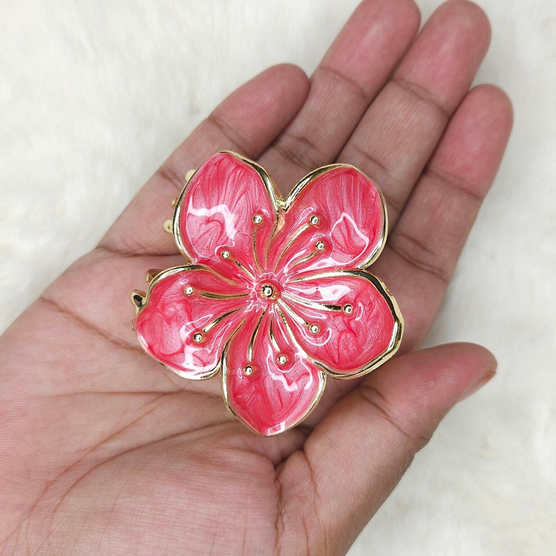Pink flower-shaped hair claw held in a hand against a white background