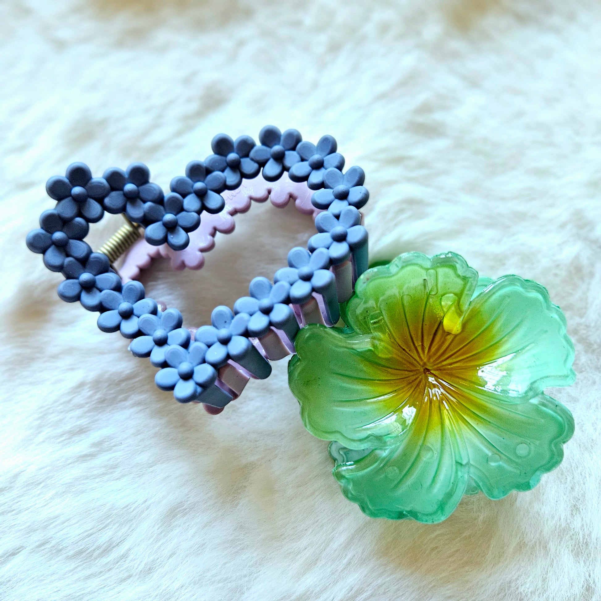 Heart-shaped hair clip with bead design and a green floral clip on a white fur background