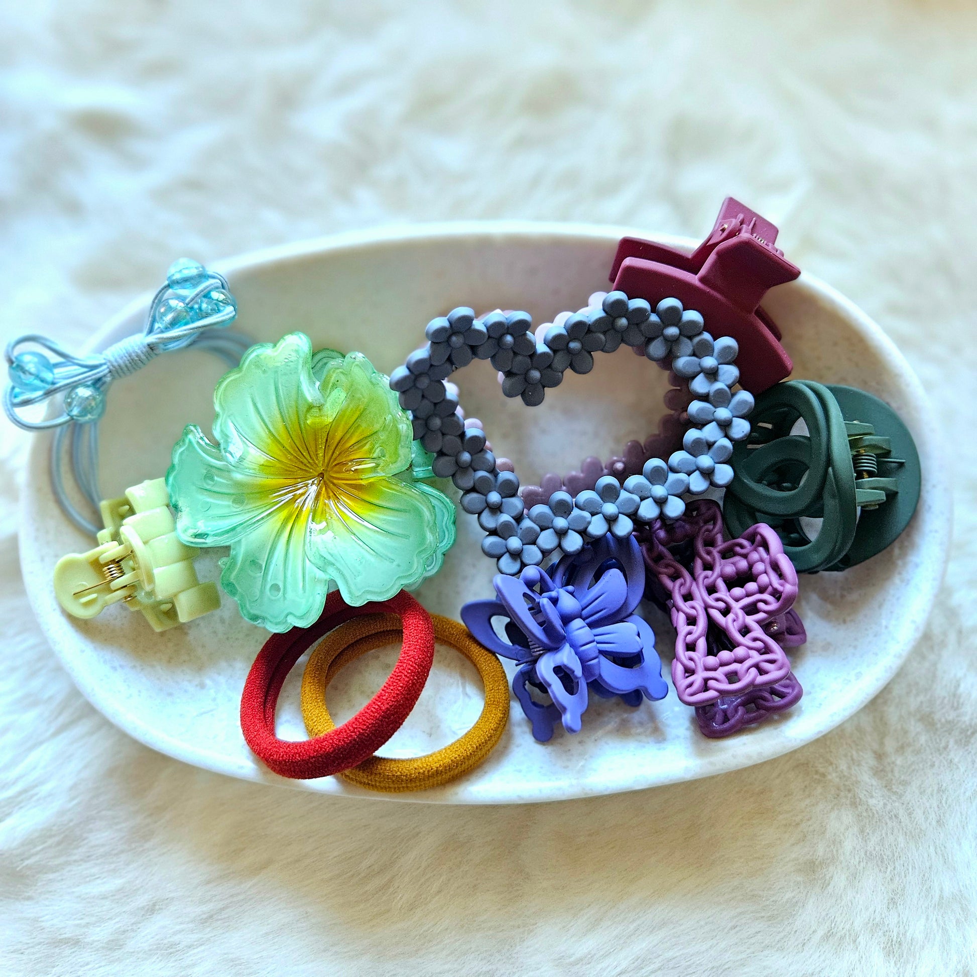 Assorted colorful hair accessories on a white plate with a white background
