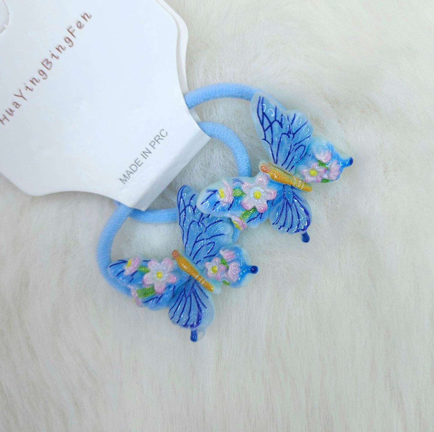 Blue butterfly-shaped hair ties with floral details on a white background