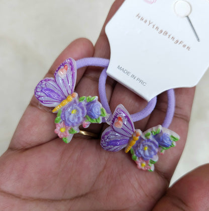 Butterfly-shaped hair ties with floral details held by a hand, branded 'Hua Ying Bingfan'.