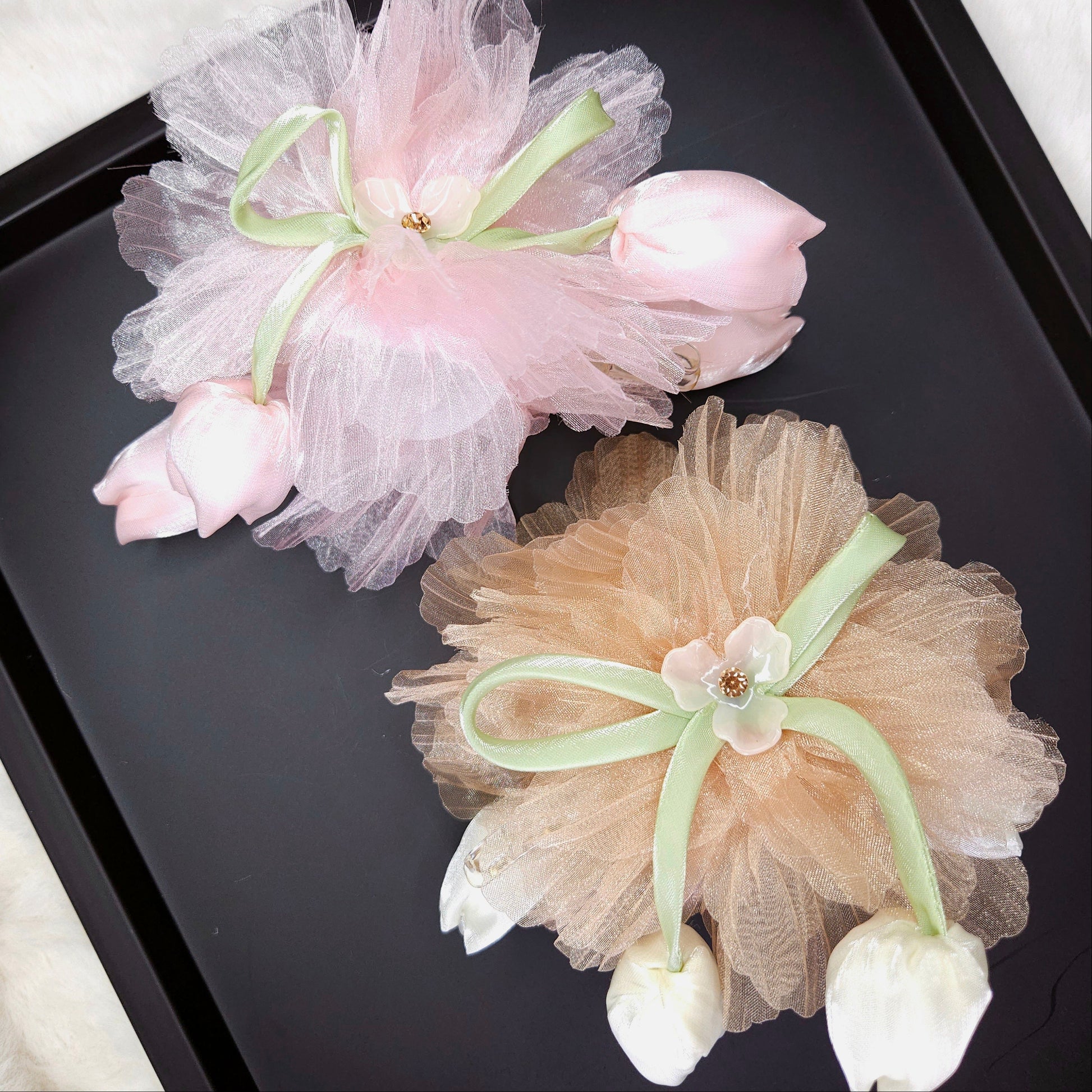 Two decorative hair accessories with tulle and flowers on a black tray.