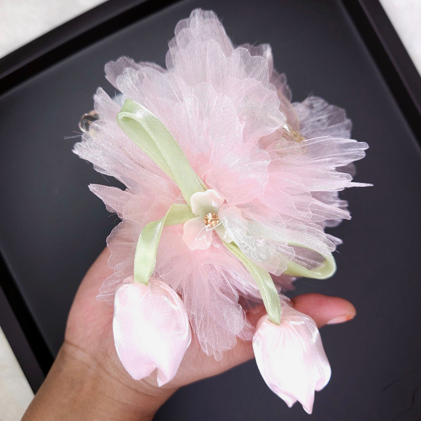 Pink floral hair accessory held by a hand on a black background