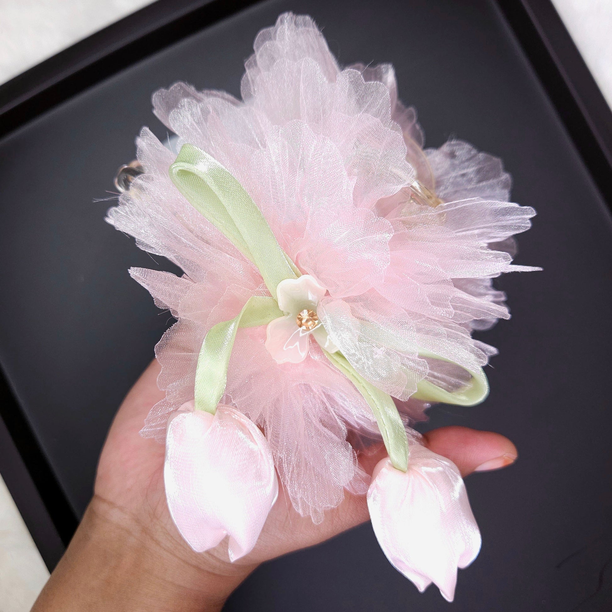 Pink floral hair accessory held by a hand on a black background