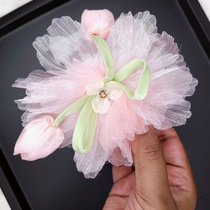 Decorative flower accessory with tulle and pink buds held by a hand on a dark surface.