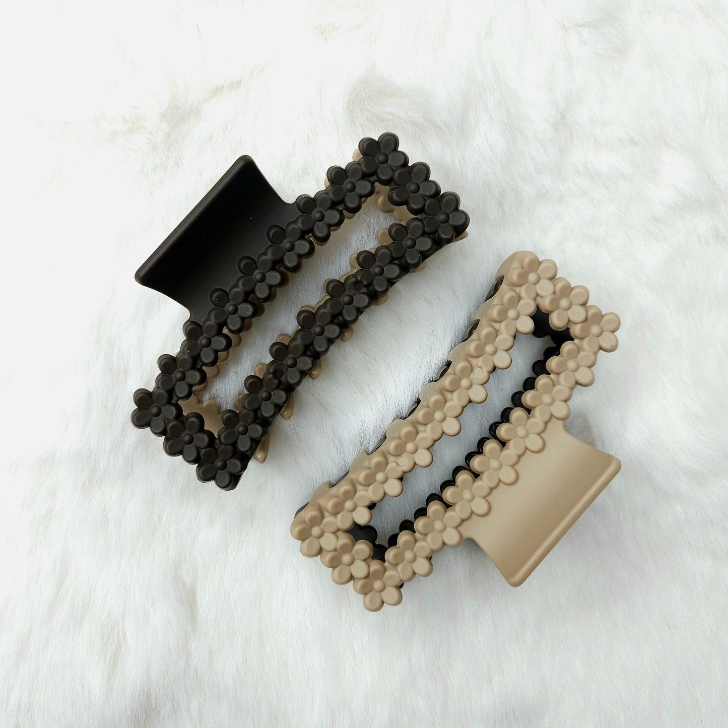 Dual tone hair claw clips, one side black and one side beige, on a white textured surface.