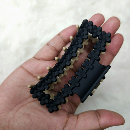 Black and beige hair claw clip held in a hand against a white background