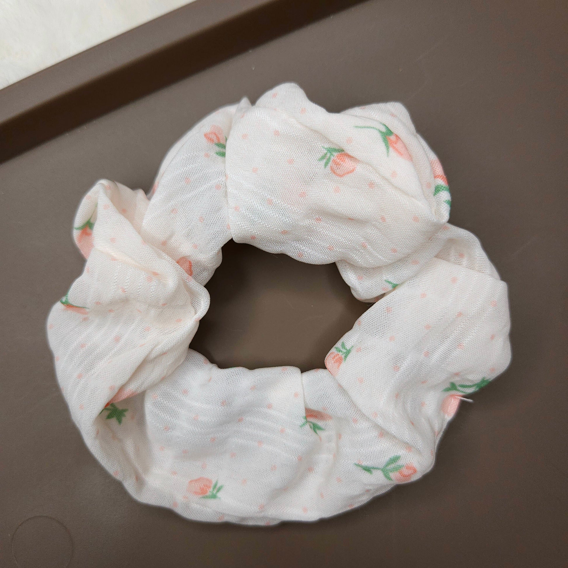 White scrunchie with orange flowers and floral pattern on a brown surface