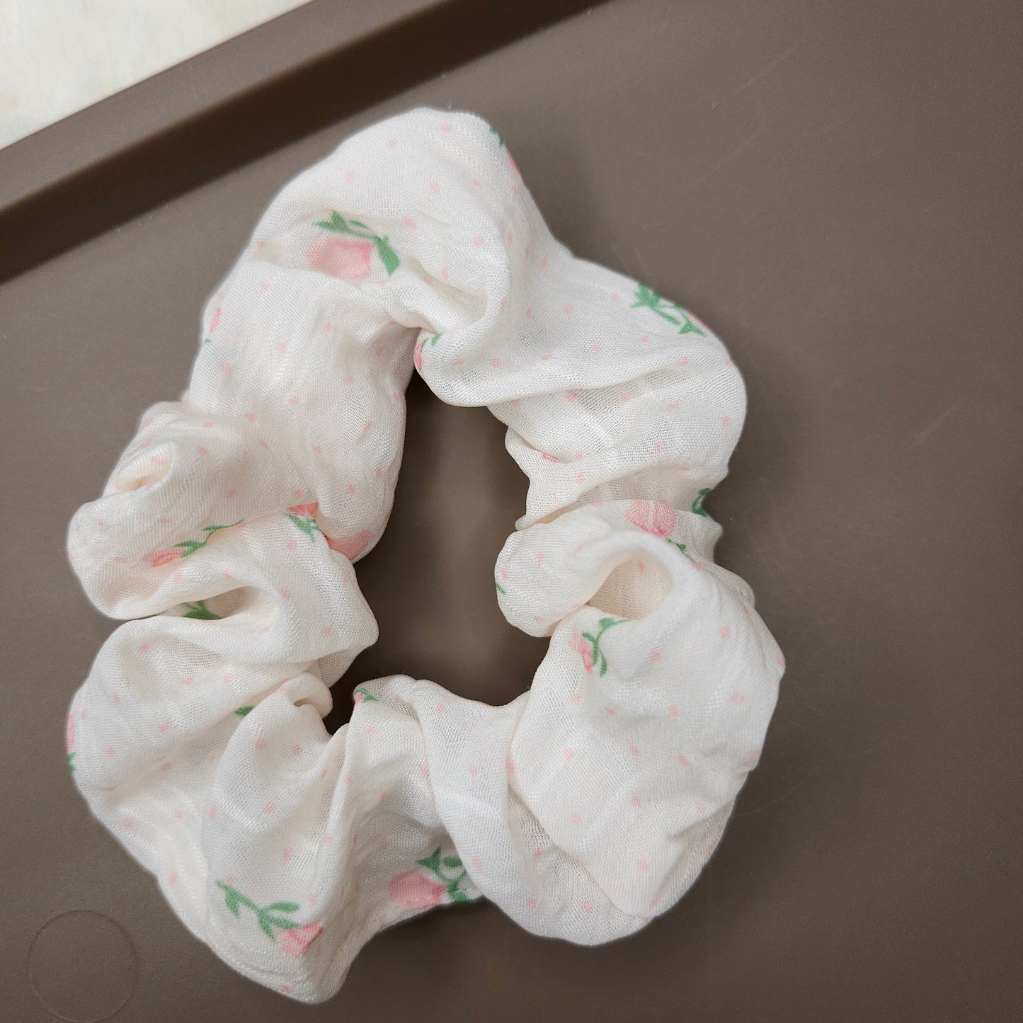 White scrunchie with pink flowers and floral pattern on a brown surface