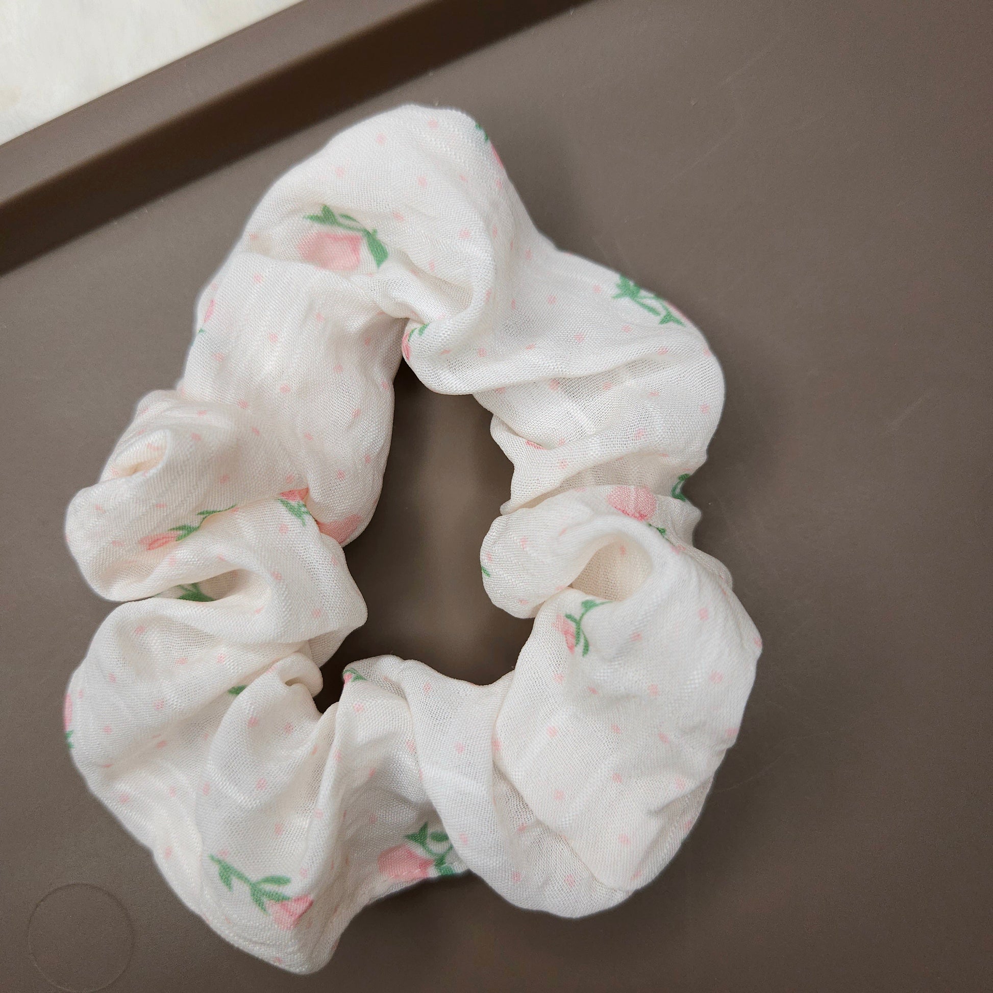 White scrunchie with pink flowers and floral pattern on a brown surface