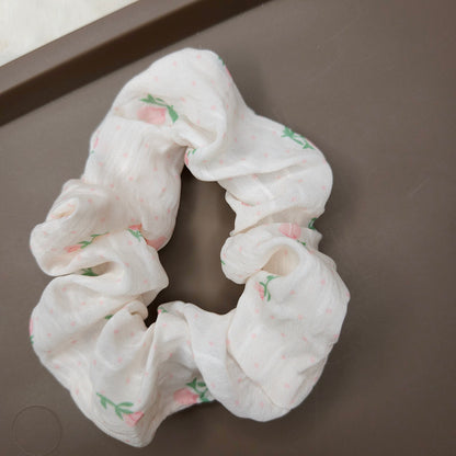 White scrunchie with pink flowers and floral pattern on a brown surface