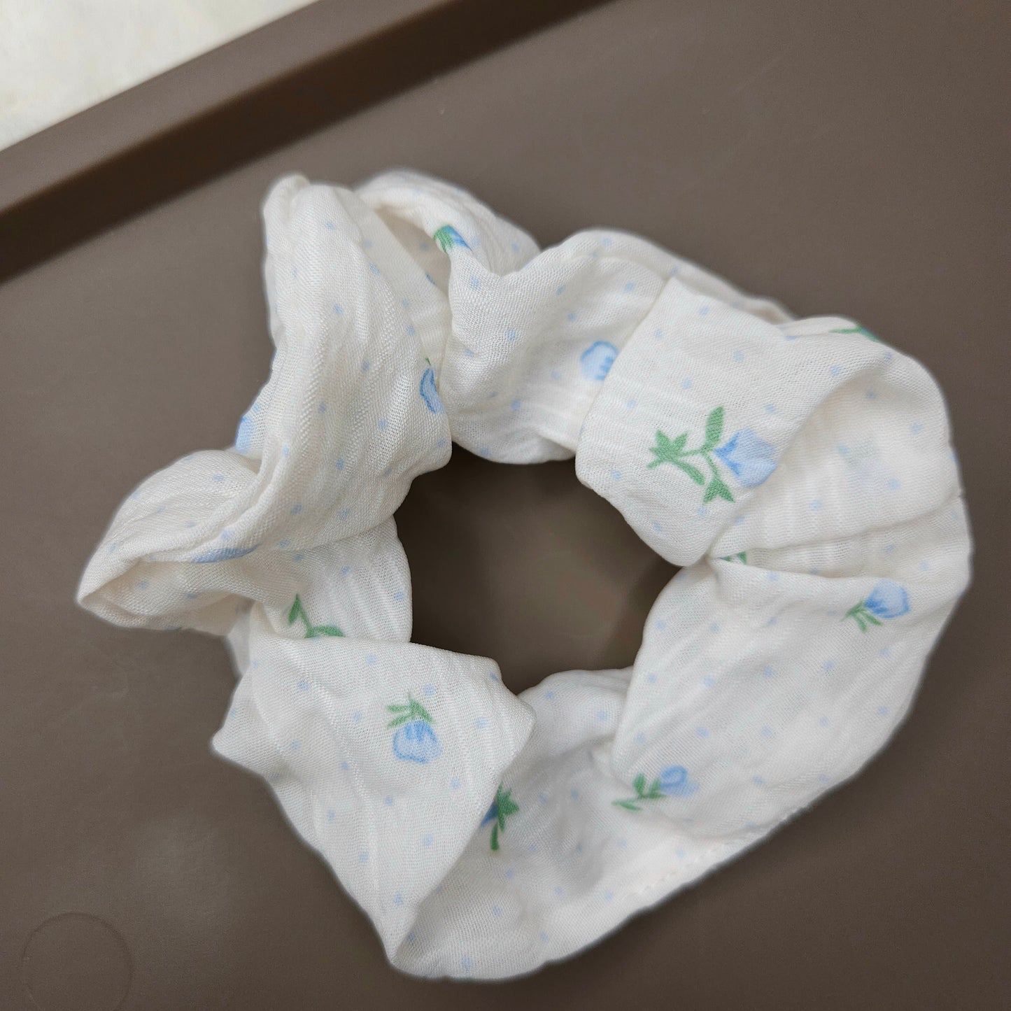 A white scrunchie with sky blue flowers and floral details.