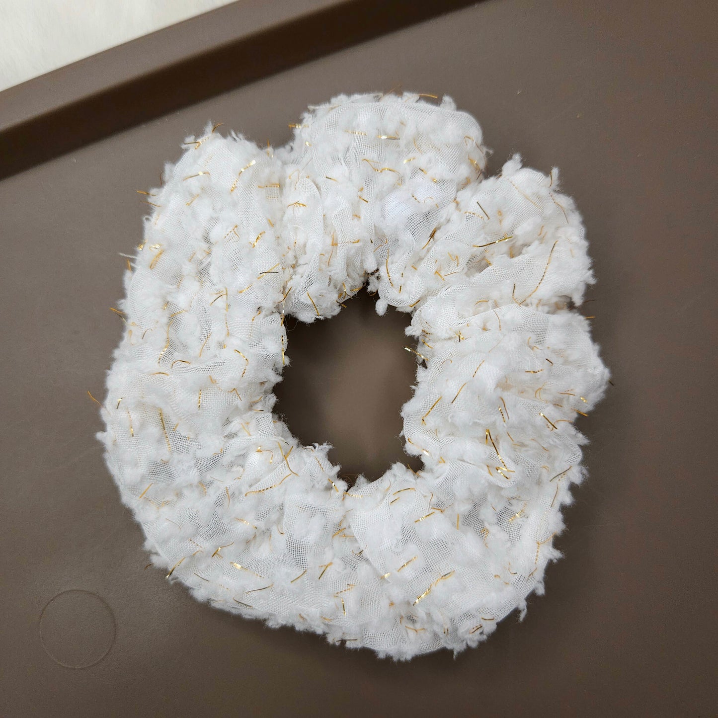 White scrunchie with floral detailing placed in a brown tray