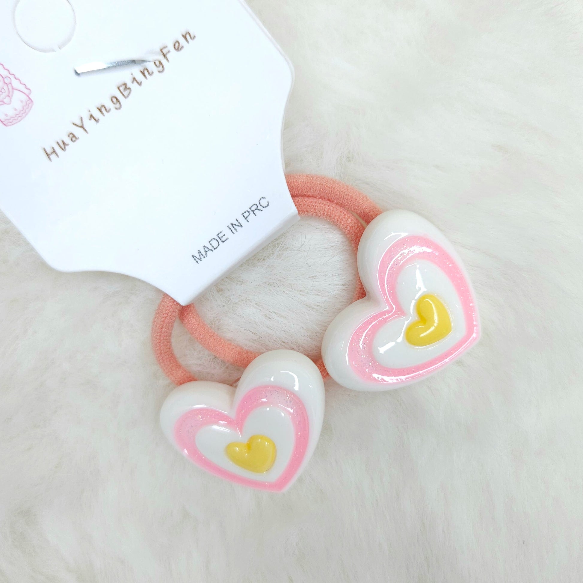 Heart-shaped hair ties with pink and white design on a beige background