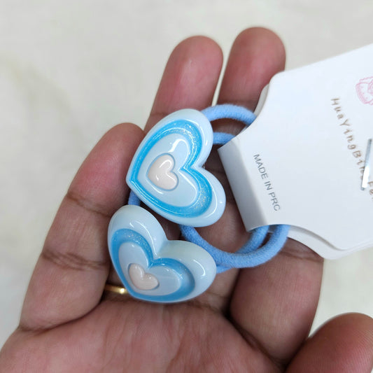 Heart-shaped hair ties with a white card labeled 'Made in PRC' held in a hand.