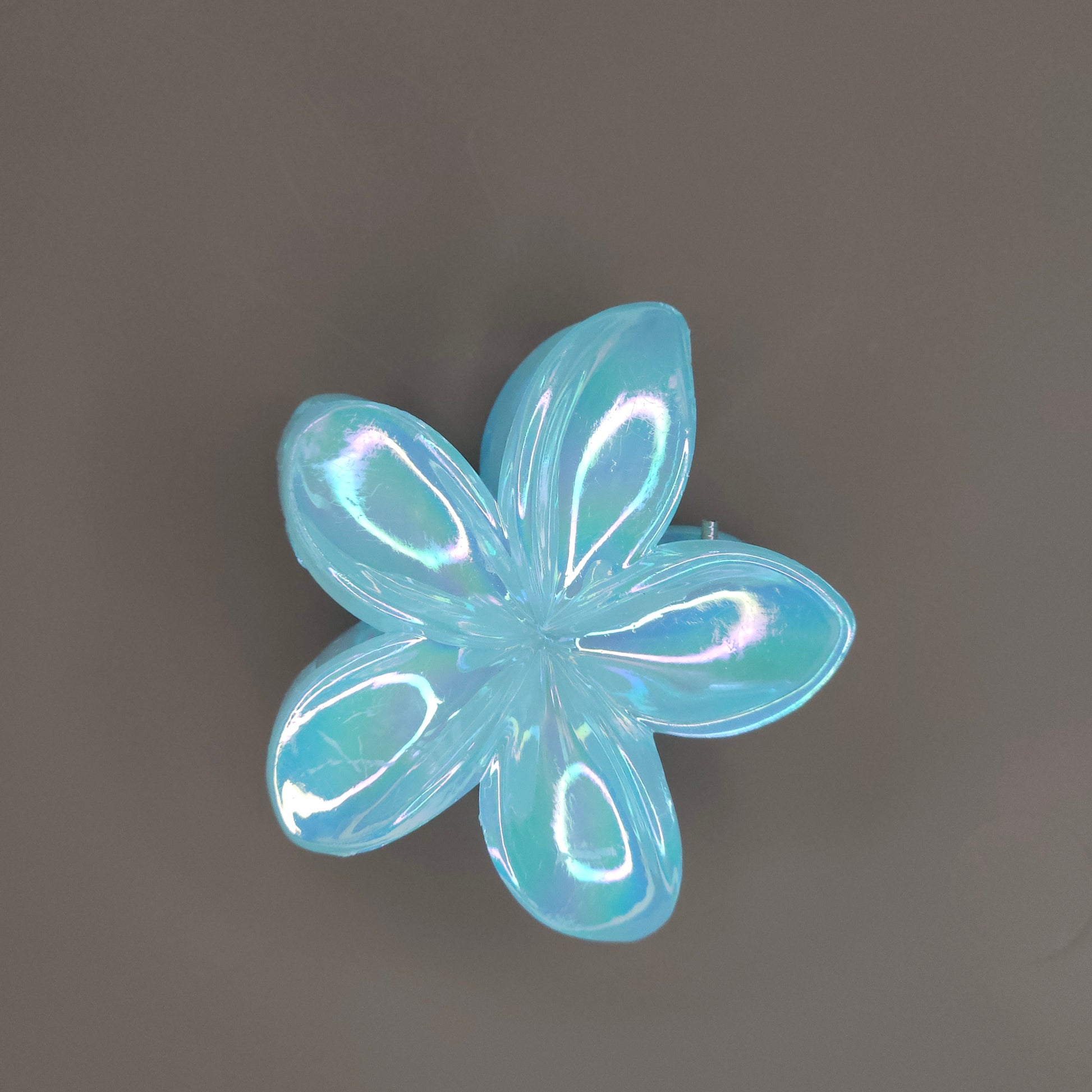 A medium-sized hair claw clip in the shape of a blooming flower, made from a lustrous sky-bluematerial that subtly shimmers in the light.
