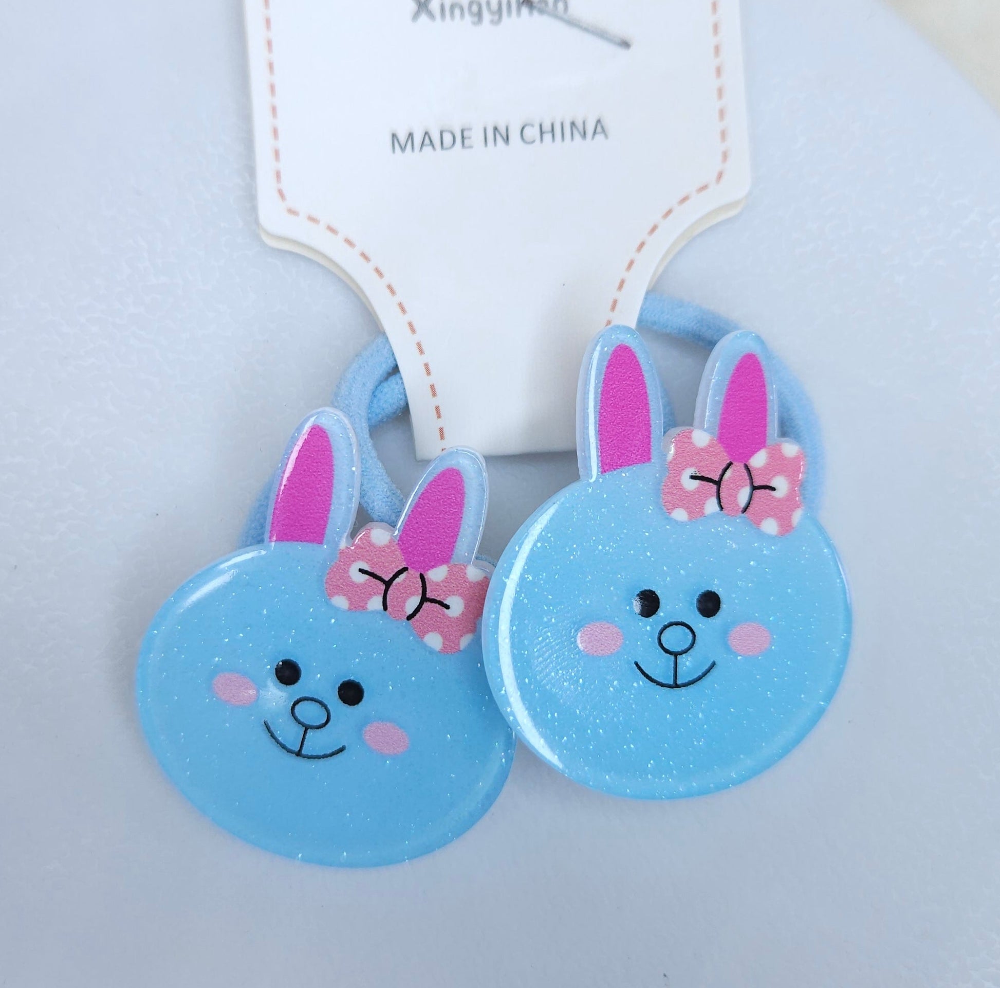 Two blue bunny-shaped hair ties with pink bows on a light gray background.