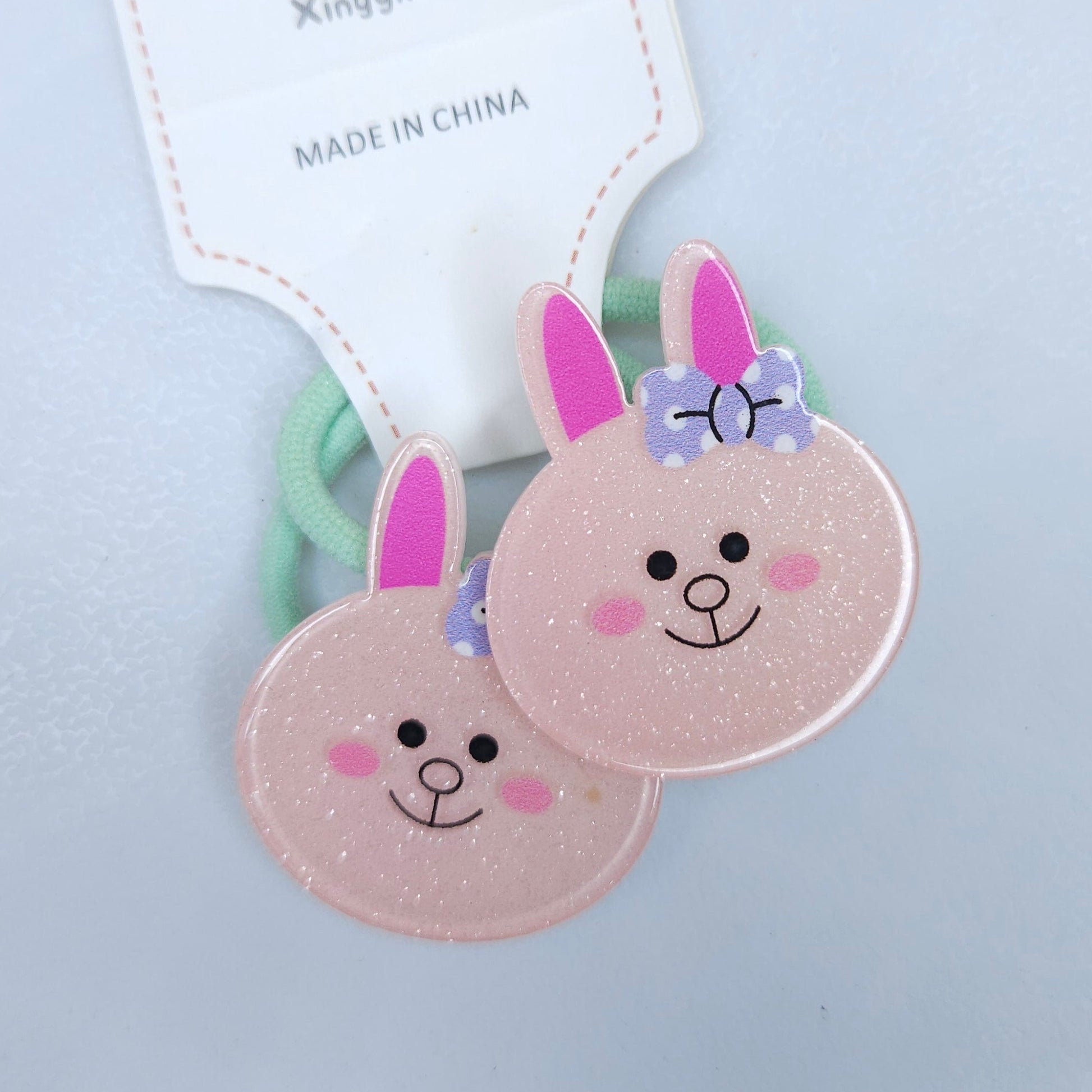 Two pink bunny-shaped hair ties with smiling faces on a light blue background.