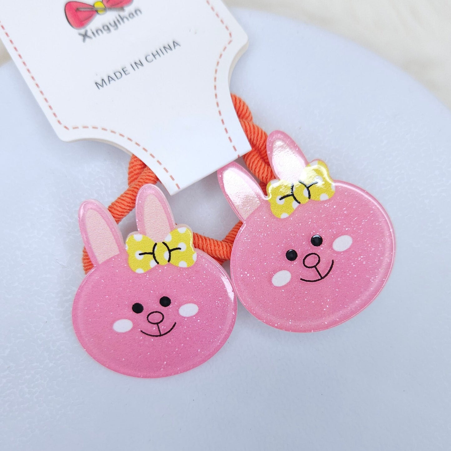 Two pink bunny-shaped hair ties with yellow bows on a white background