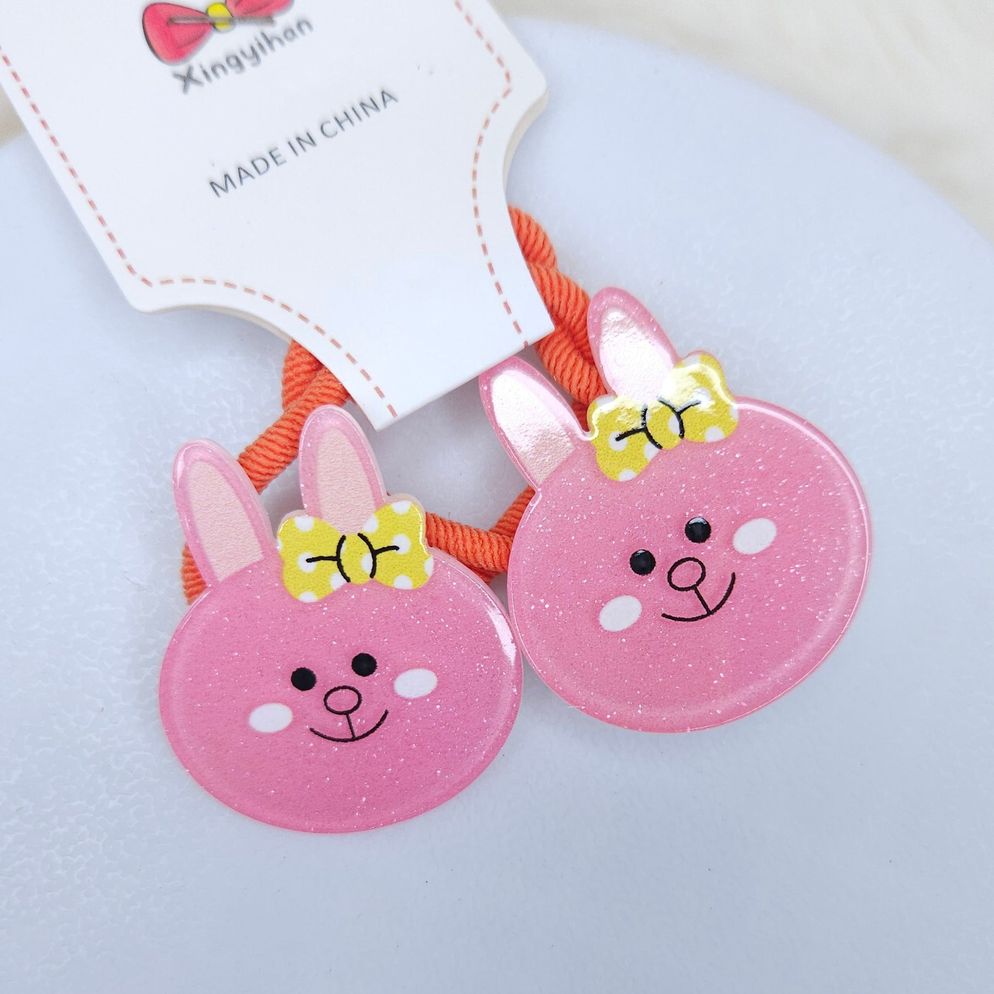 Two pink bunny-shaped hair ties with yellow bows on a white background