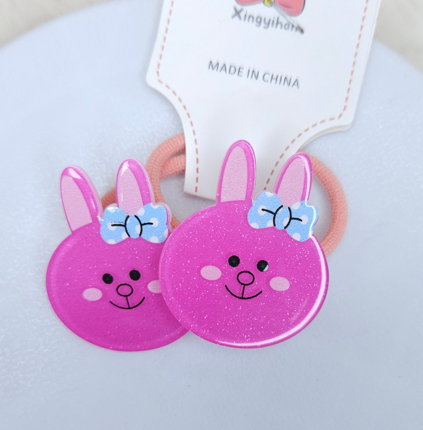 Two pink bunny-shaped hair ties with blue bows on a white background