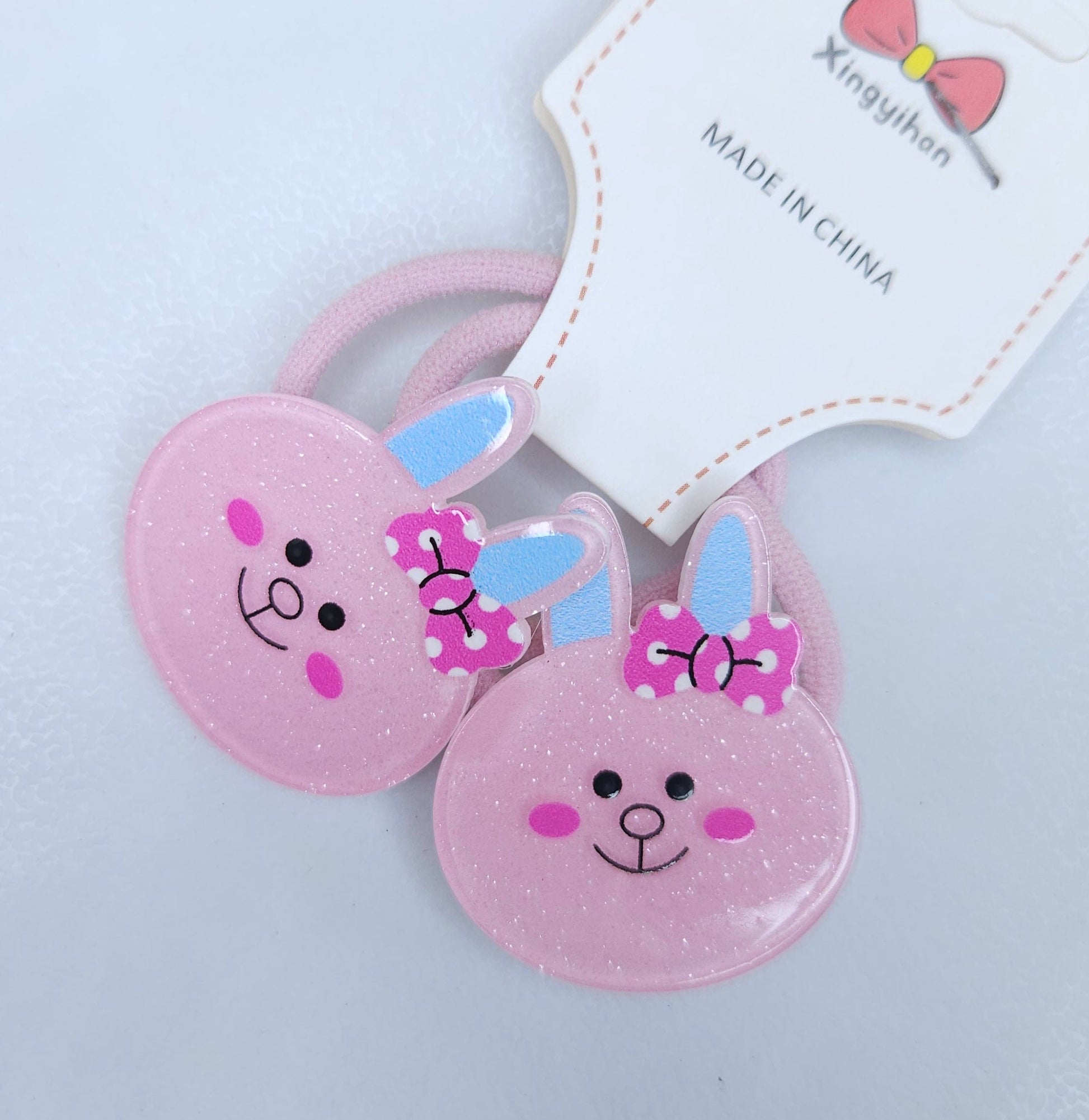 Two pink bunny-shaped hair ties with a tag on a light gray background