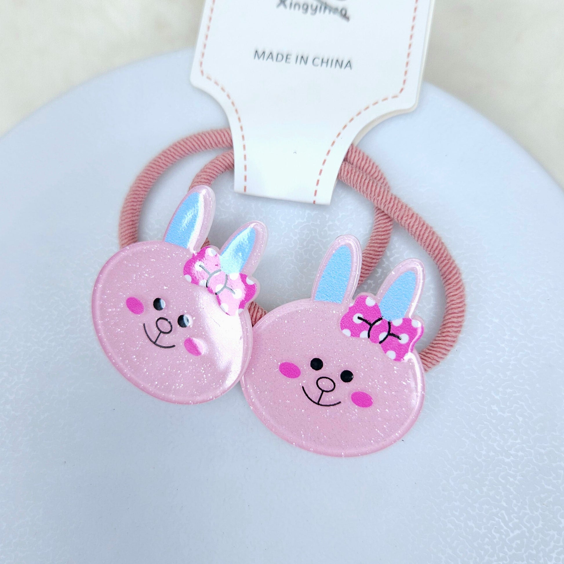 Two pink bunny-shaped hair ties with a bow on a light gray background