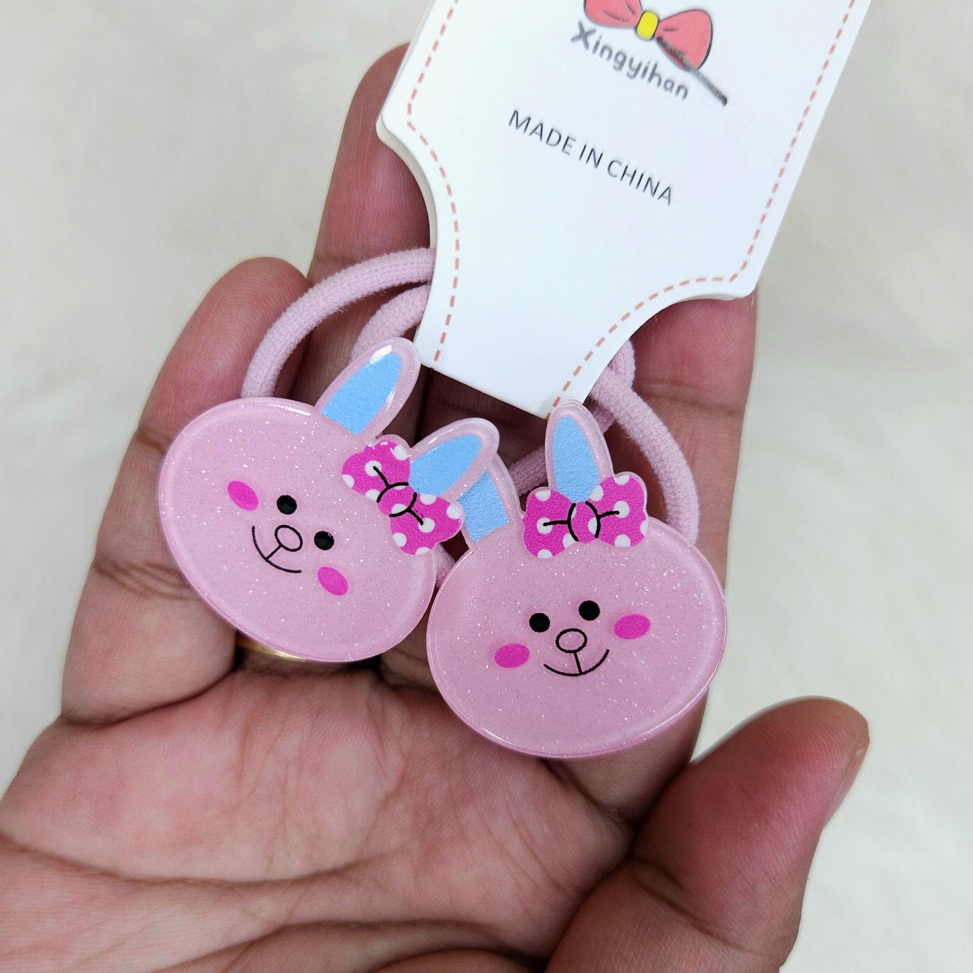 Pink bunny-shaped hair ties with a visible brand label held in a hand.