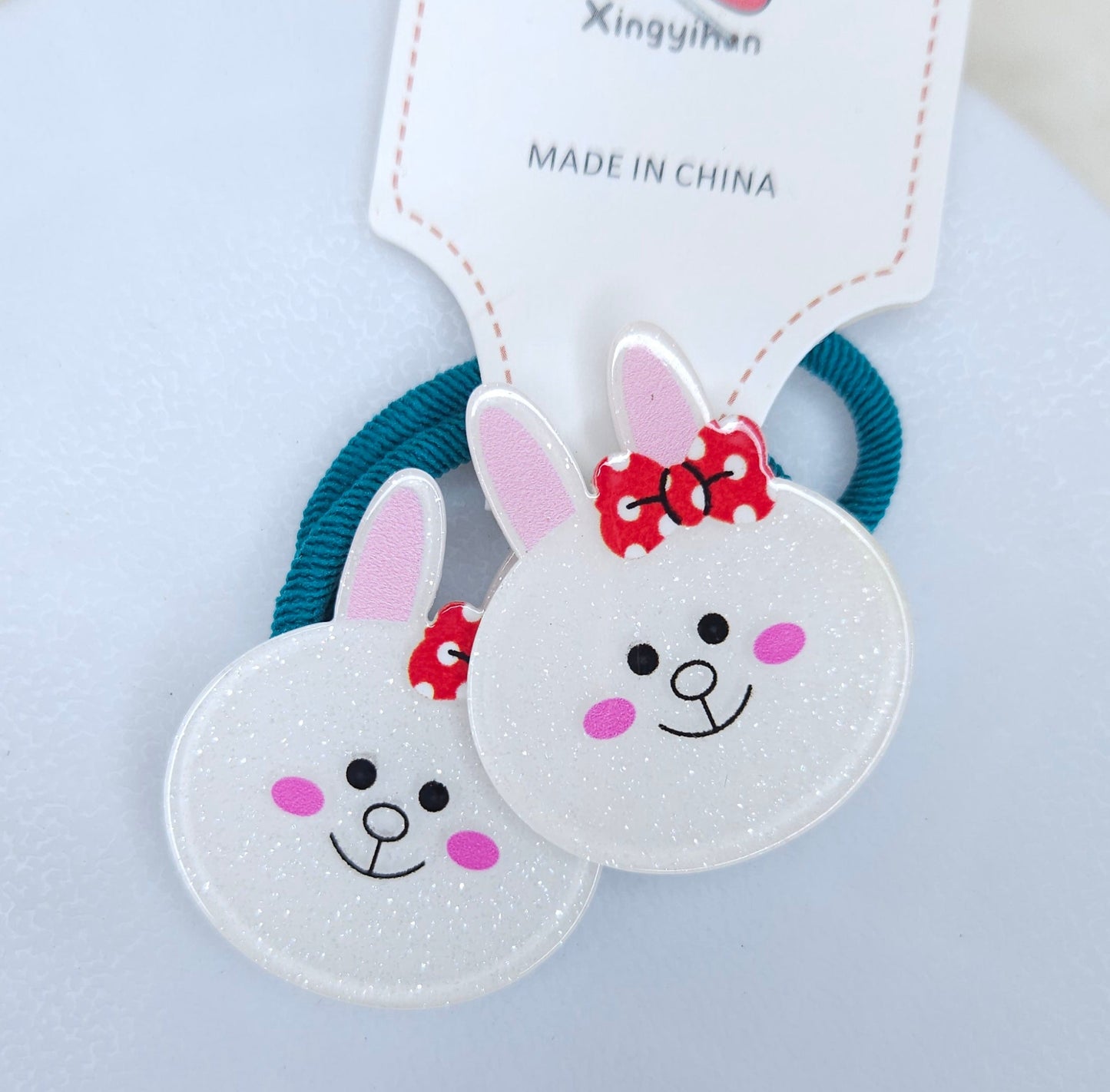 Two cartoon rabbit hair ties with a branded tag on a light gray background