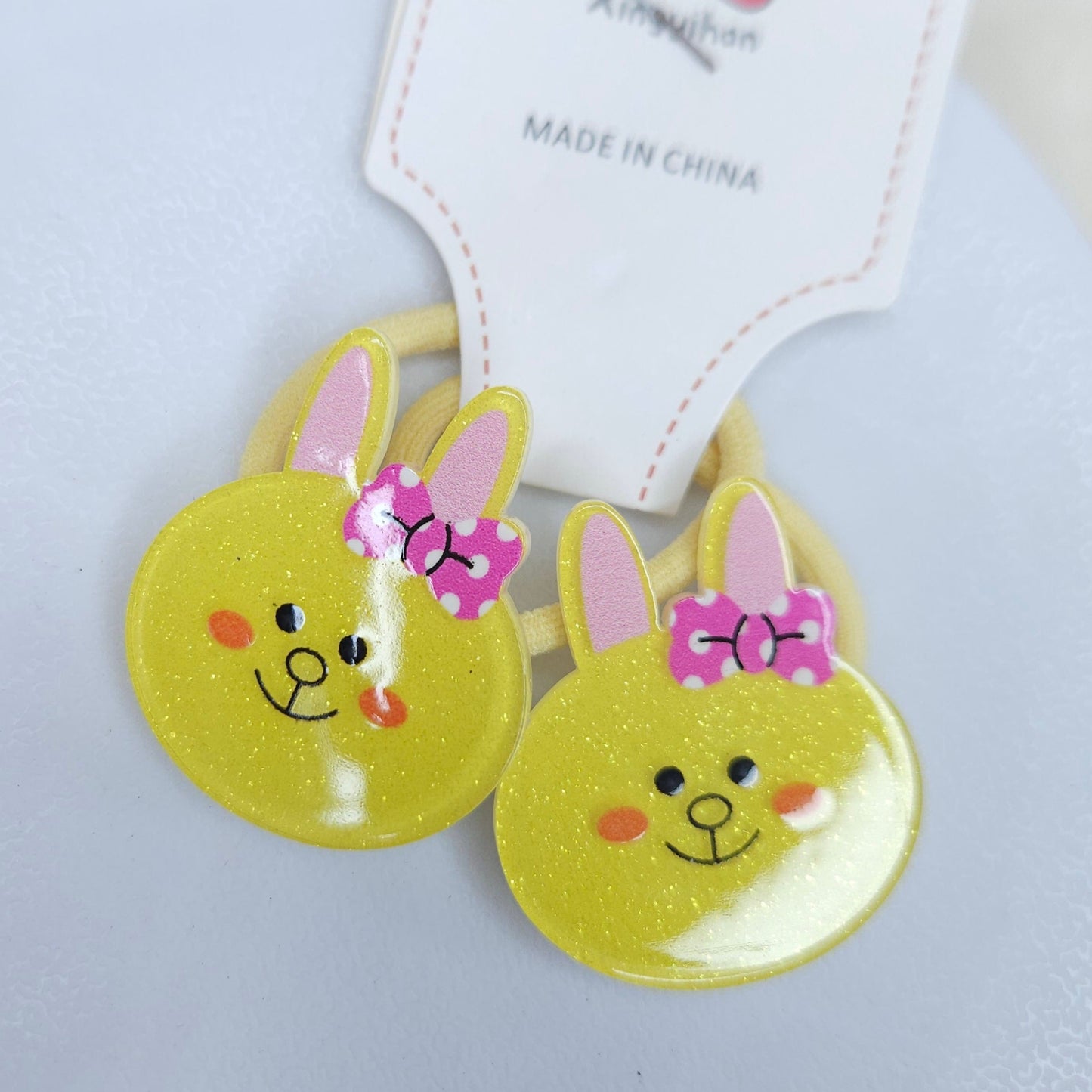 Two yellow bunny-shaped hair ties with pink bows on a white background