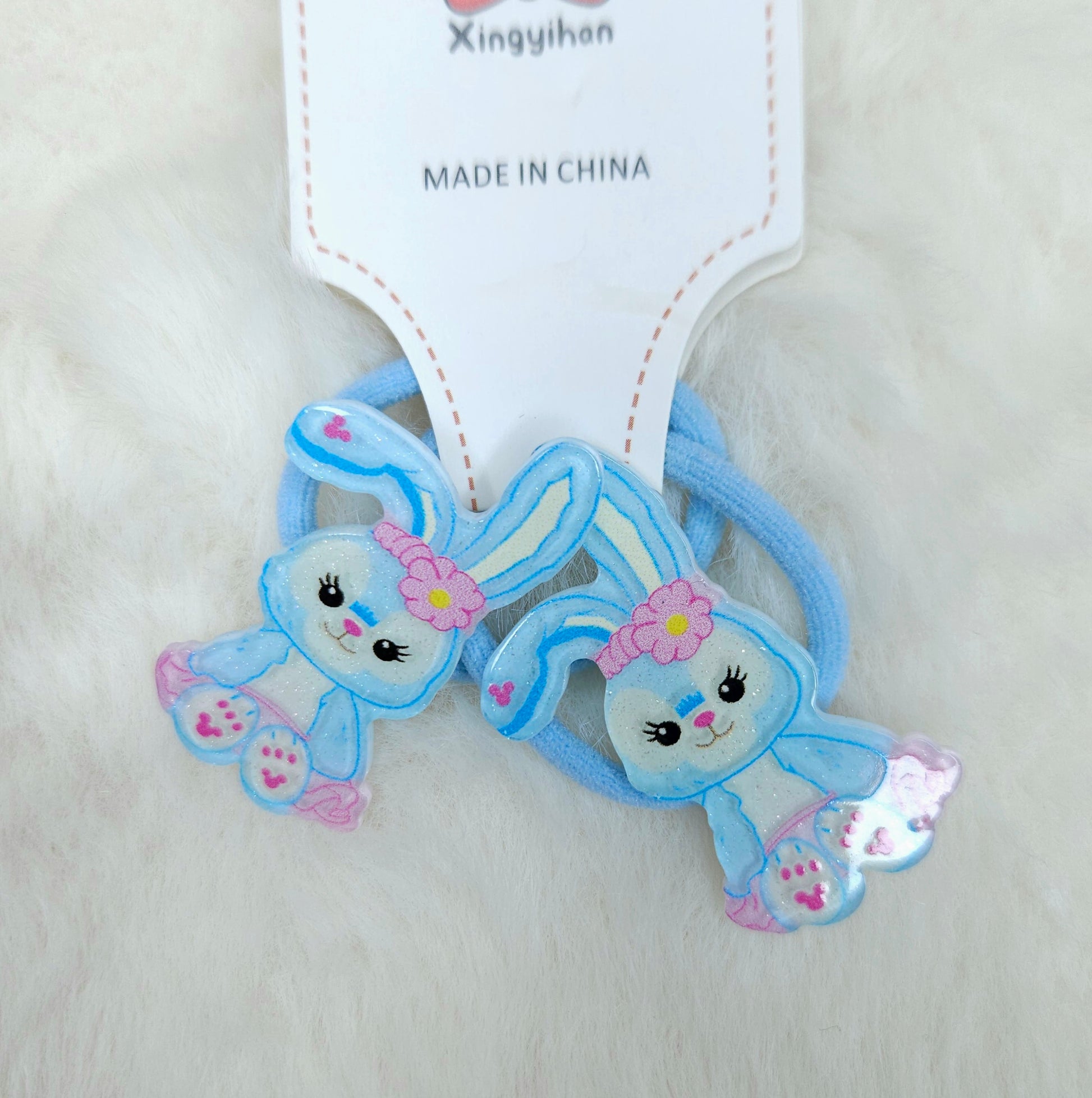 Two blue cartoon character hair ties with pink flowers on a white background, branded 'Xingyihan'.