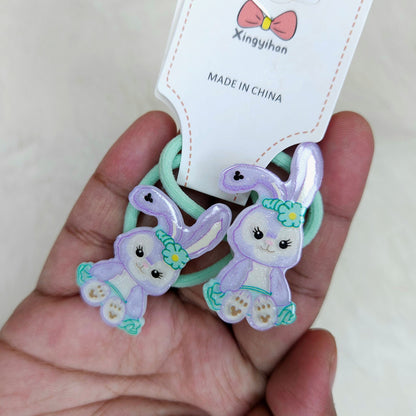 Two purple bunny-shaped hair ties held by a hand with a visible brand label.