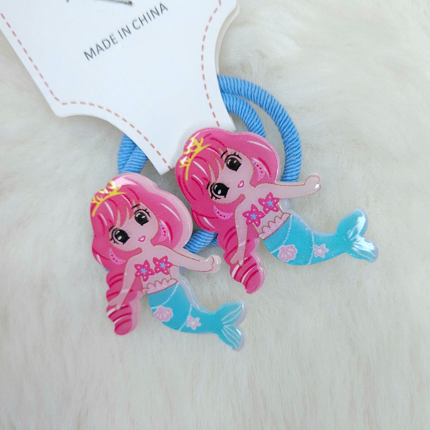 Two mermaid-themed hair ties with pink hair and blue tails on a light background.