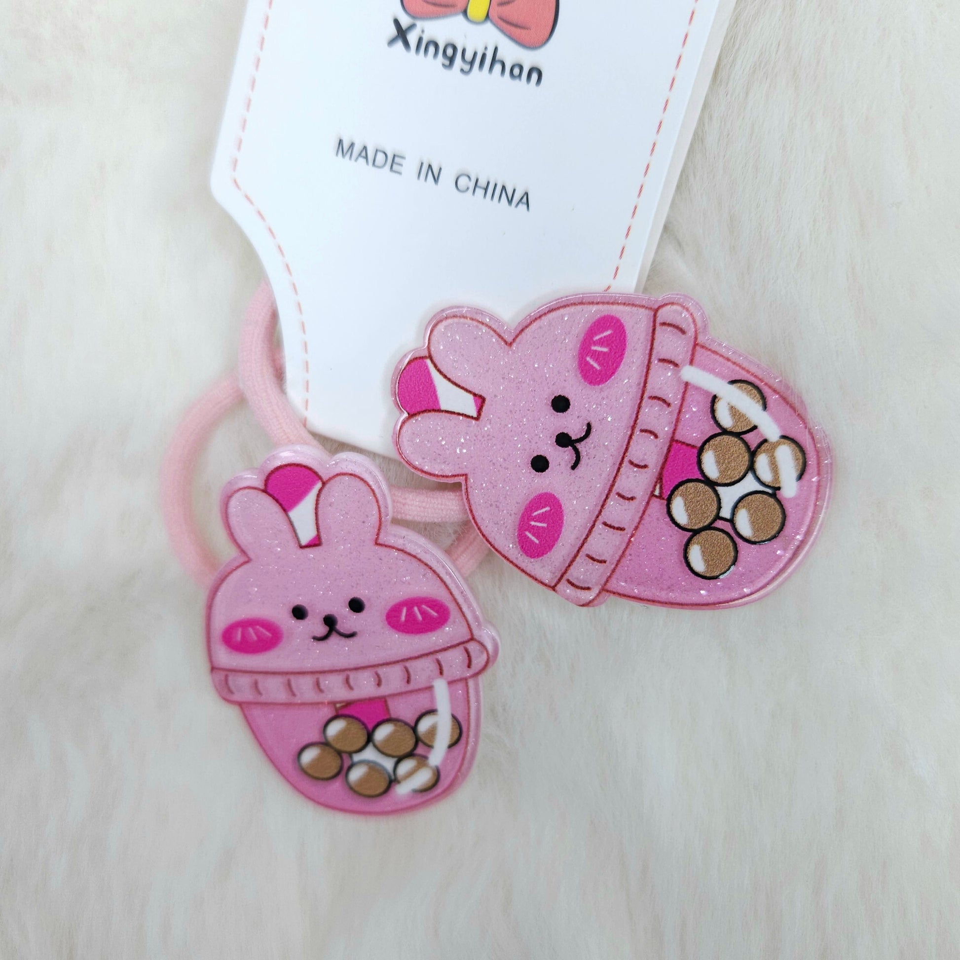 Pink bunny-shaped hair ties with a tag labeled 'Xingyihan' on a light background